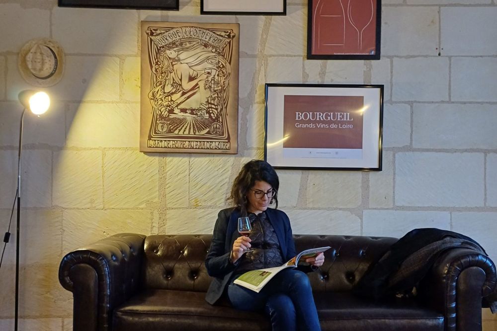Lectrice dégustant un verre de Bourgueil, affiches de l'appellation au mur